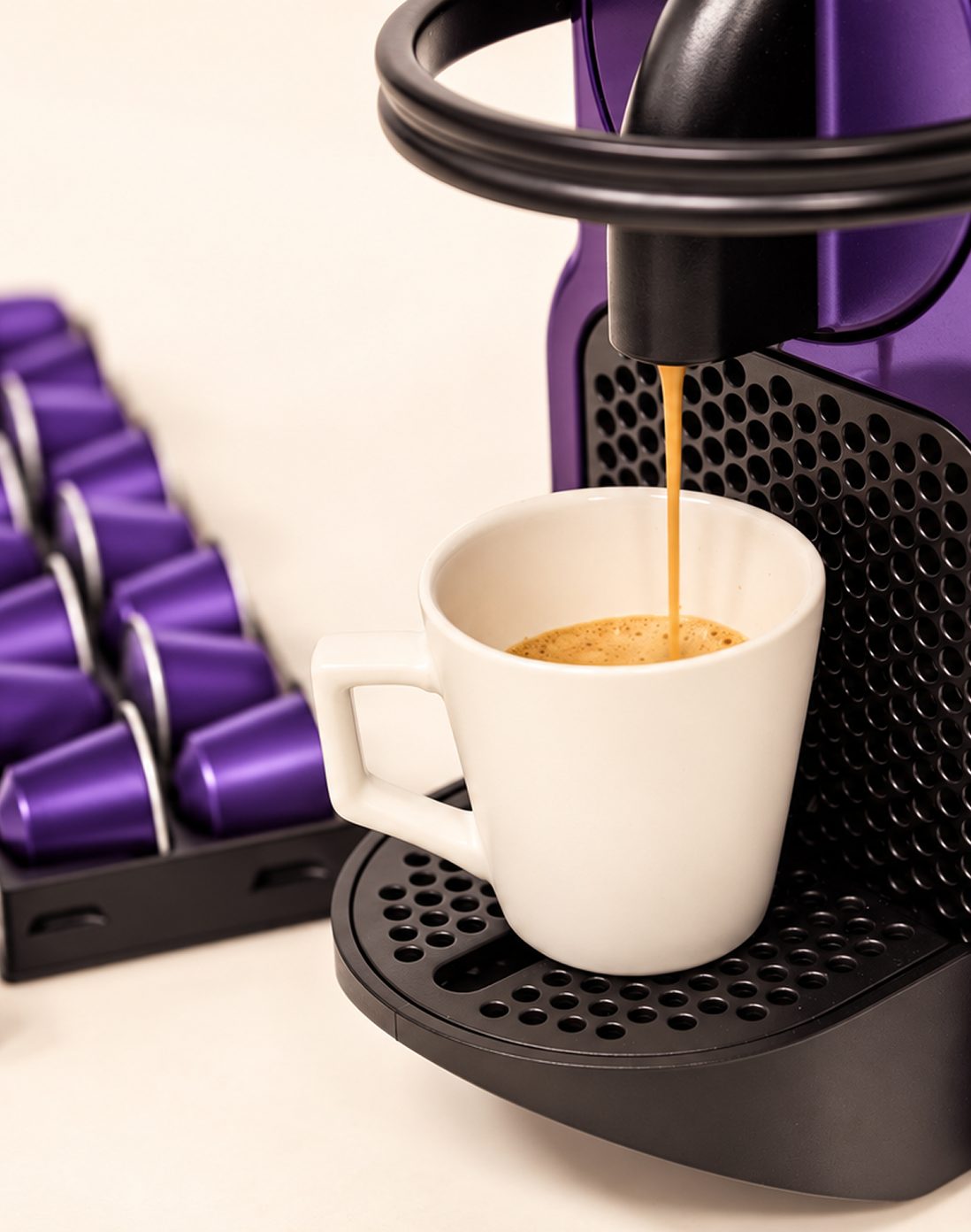Un café qui coule dans une tasse blanche sous une machine à capsules violette, un porte-capsules rempli de capsules Mush Caps à côté