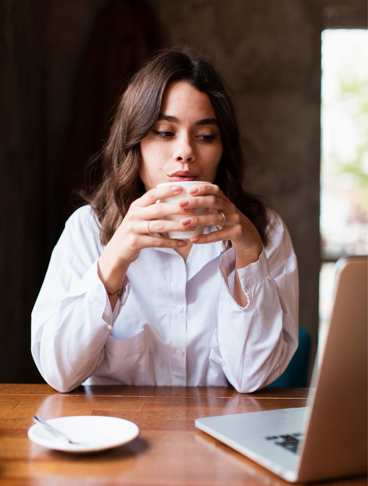 Une femme tient sa tasse de café à deux mains devant son ordinateur