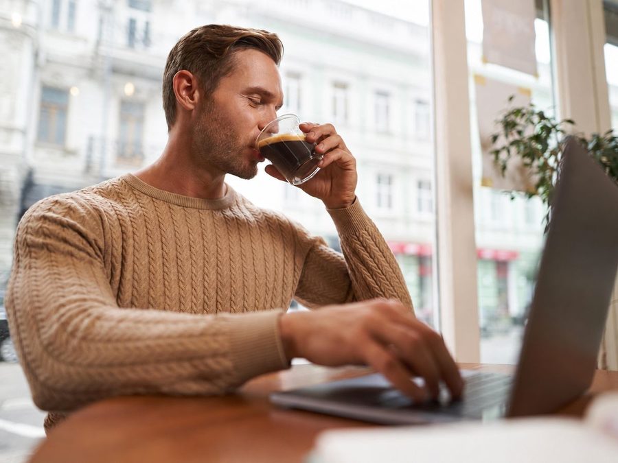 Un homme boit son café devant son ordinateur, dans un café
