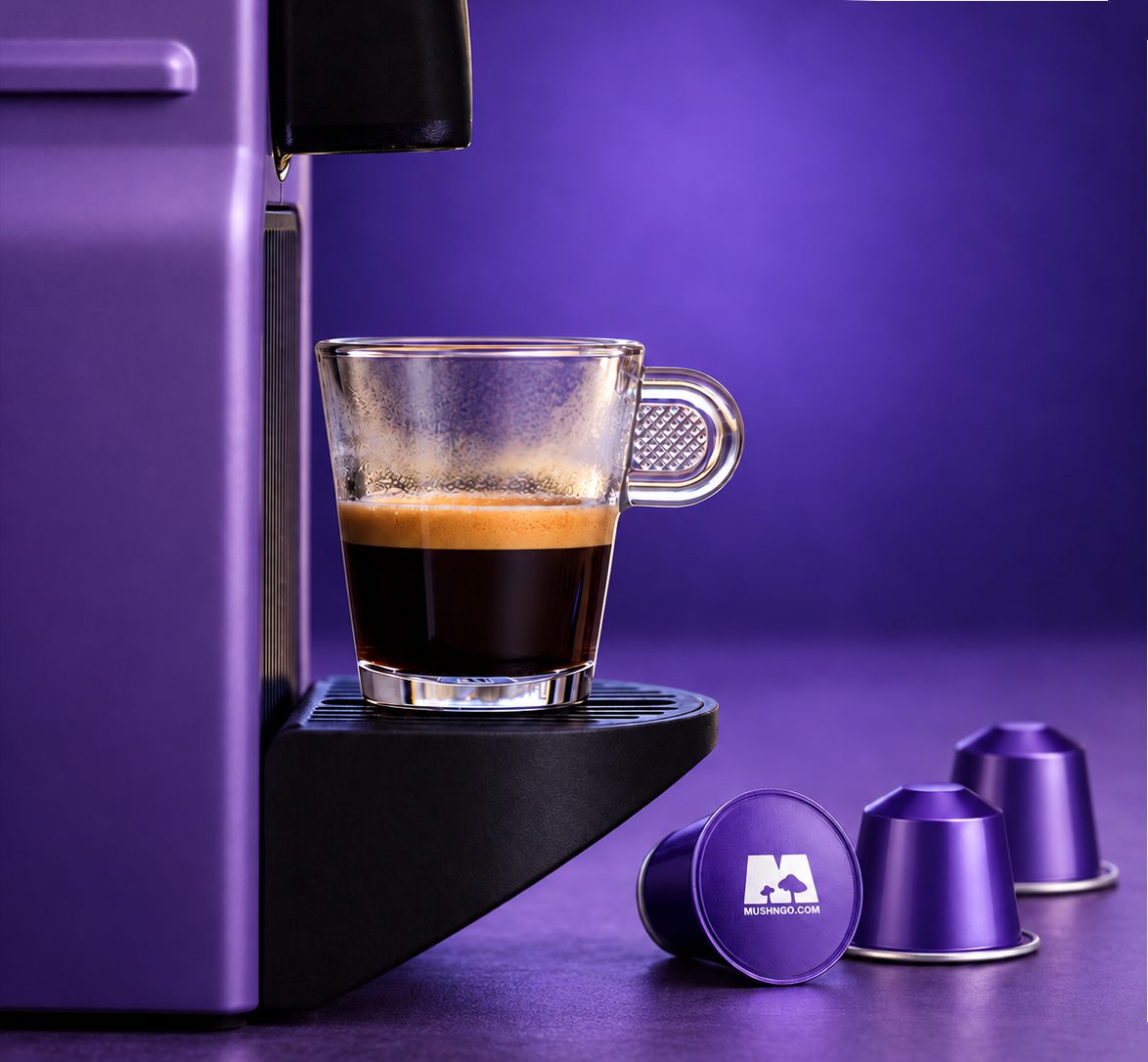 Un espresso dans une tasse en verre sous une machine à capsules violette, trois capsules Mush Caps posées à côté