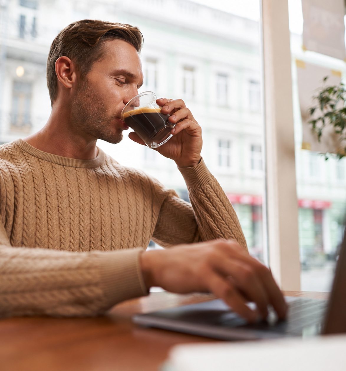 Un homme boit son café devant son ordinateur, dans un café