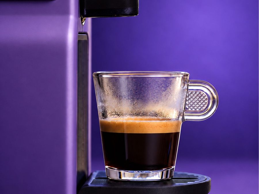 Un espresso et sa mousse dans un verre, sous une machine à capsules violette