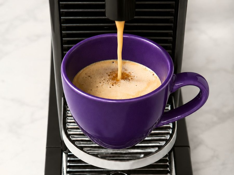 Vue de dessus d'une tasse violette sous la machine, le café qui coule et sa mousse