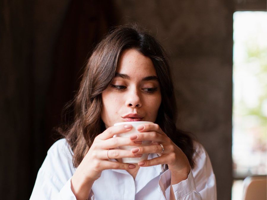 Une femme tient sa tasse de café à deux mains devant son ordinateur